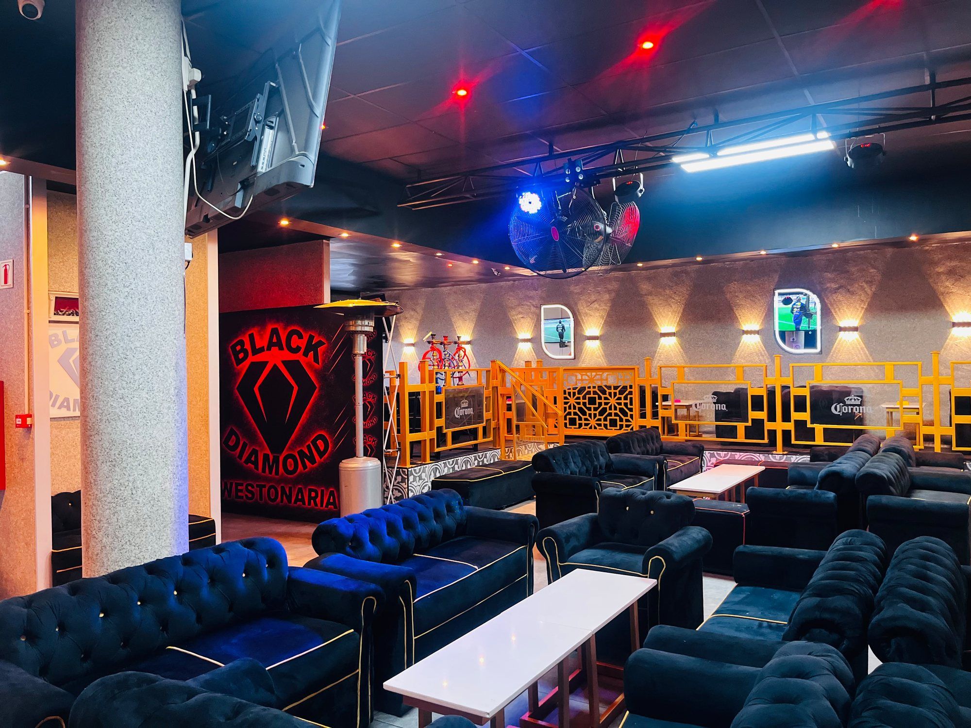 The main floor lit in red and blue, with the glowing BLACK DIAMOND WESTONARIA mural on the far wall, a lighting rig and industrial fans overhead, and rows of black buttoned velvet couches in the foreground.